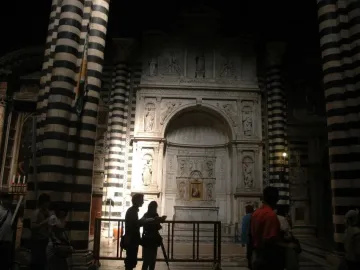 Piccolomini Altarpiece inside a dimly lit church with black-and-white striped columns and visitors nearby.