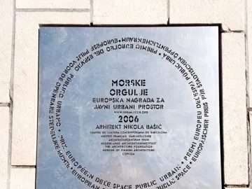 Commemorative plaque for the Sea Organ embedded in light-colored paving stones, with hiking shoes visible at the bottom.