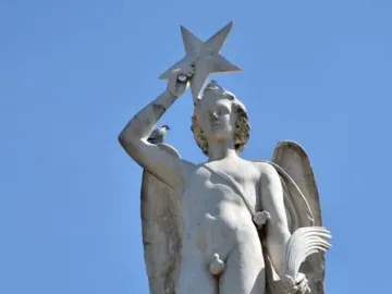 Weathered marble figure atop the Genio Catalán Fountain, holding a star overhead with pigeons perched on the base and shoulder.