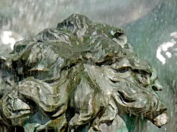 Close-up of a weathered bronze head from the Monument aux Girondins, with curly hair and water flowing over the face.