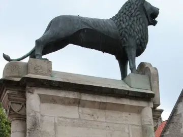 The Brunswick Lion statue on a stone pedestal, with two people holding white and black T-shirts below it.