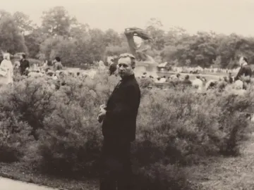 The Chopin Monument stands in a park with a crowd gathered around it and a man in a suit in the foreground.