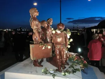 Kindertransport bronze sculpture of several children with suitcases on a plinth, decorated with flowers.