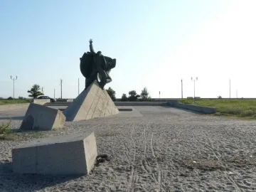 Monument of Eupatoria Assault showing three bronze figures on a large triangular concrete pedestal in a paved square.