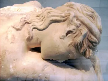 Close-up of the head and upper torso of the Sleeping Maenad marble sculpture, with wavy hair and a tilted resting pose.