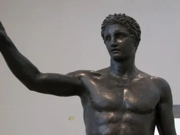 The Antikythera Ephebe bronze statue shown from the chest up, with curly hair and one arm raised.