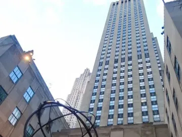 Atlas sculpture showing a kneeling muscular man holding up an armillary sphere in front of skyscrapers.