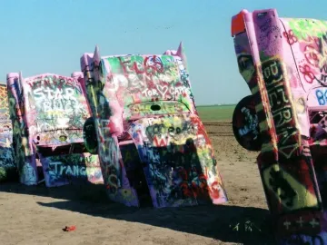 Cadillac Ranch with several vintage Cadillacs buried nose-down in a dusty field and covered in colorful graffiti.
