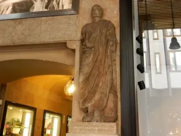 Scior Carera stone relief of a draped male figure set into a column beside a glass storefront.