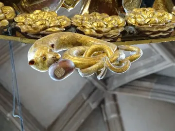 Close-up of the gilded serpent detail on the Angelic Salutation, holding a nut-like object in its mouth.
