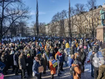 Johan Ludvig Runeberg Statue overlooking a large crowd gathered in a snowy Helsinki park.