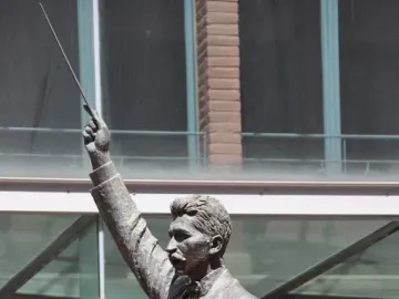 A bronze statue of Lluís Millet with a mustache, wearing a suit and bow tie and raising a conductor\'s baton.