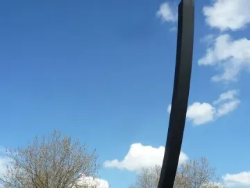 The Arc de 124,5° sculpture rises against a blue sky with clouds in Berlin.