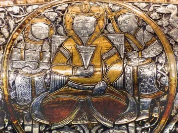 Circular medallion from the Baptistery of Saint Louis showing a central ruler holding a cup, flanked by two attendants, with silver foliage and small animals around the base.
