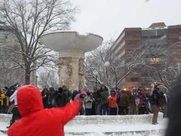 Dupont Circle Fountain partially covered in snow with people gathered around it in a winter park.
