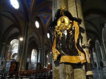 Memorial to Maria Raggi mounted on a marble pillar inside a church interior with painted ceilings and pews.