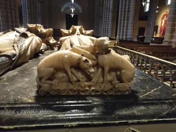 Detail of the Tomb of Charles III and Eleanor showing two sculpted dogs at the base of the monument, with draped stone effigies behind them.