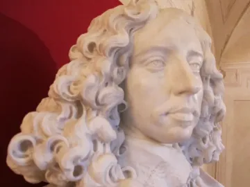 Marble bust of Francesco I d\'Este with curly hair, draped clothing, and an ornate pedestal against a black background.
