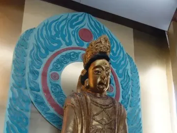 A gilded seated statue with a crown and ornate robes displayed against a carved blue and red backdrop at Huangze Monastery Rock Sculptures.