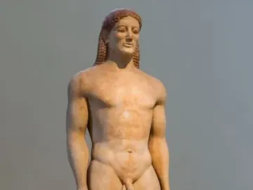 Kroisos Kouros, a nude ancient male statue with braided hair and a slight smile.
