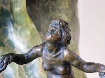 Bronze nude figure from The Wave with outstretched arms against green veined stone.