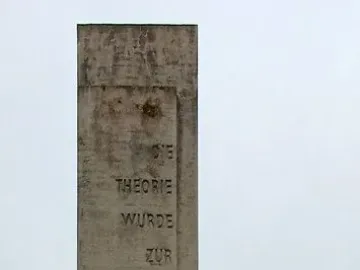 Karl Marx Monument with a carved stone stele and a dark bust on a pedestal in a park setting.