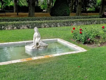 White Mermaid Fountain statue pouring water into a rectangular stone basin in a green park.