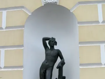 Apollino nude male statue in a white arched niche with a quiver and tree trunk support.