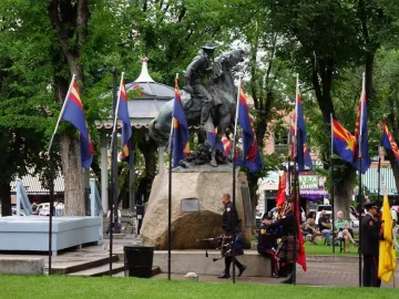 Buckey O\'Neill Monument with a bronze equestrian statue surrounded by flags and people at a ceremony.