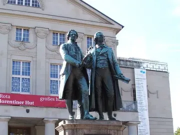 Goethe and Schiller Monument on a tiered stone pedestal in front of a theatre building.