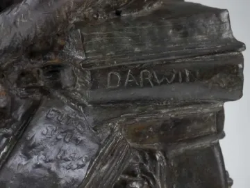 Close-up of Hugo Rheinhold’s Ape With Skull sculpture showing a stack of books with DARWIN on the spine.