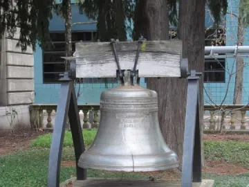 The Liberty Bell displayed on a wooden platform with a dark metal frame, surrounded by trees and ground cover.
