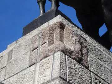 Stone plinth of the Grunwald Monument with red and grey panels, seen from below with the bronze legs of the equestrian statue above.