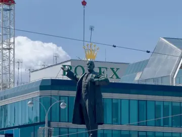 Lenin Monument on a stone pedestal with a modern glass building behind it