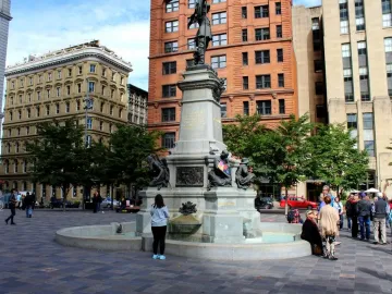 The Maisonneuve Monument stands in a paved square, with a tall stone column topped by a dark statue and smaller figures at the base fountain.
