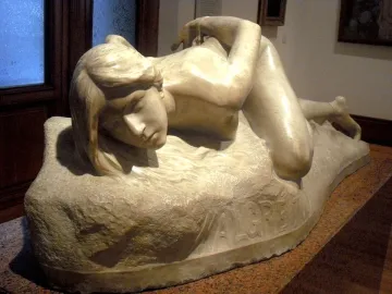 Malgré Tout, a light-colored stone sculpture of a reclining nude female figure on a rough base with the inscription \