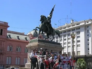 Manuel Belgrano equestrian statue on a tall pedestal in a city square, with people gathered around the base.