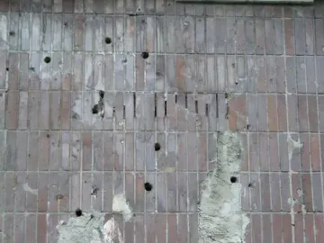 Worn Plon relief wall with reddish-brown vertical tiles, missing patches, and white residue