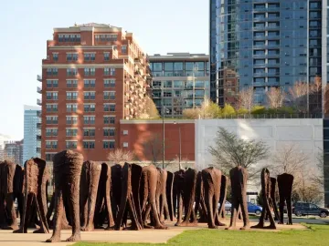 Agora sculpture in Grant Park, with tall dark headless figures standing on a paved and grassy area against Chicago buildings.