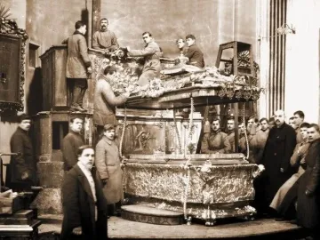 Men dismantle the ornate Alexander Nevsky reliquary on a raised platform in a black-and-white photograph.