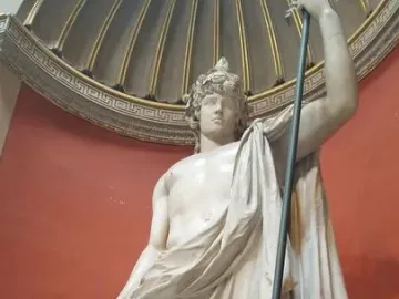 Antinous Braschi, a white marble statue of a youthful male figure with a bare torso, draped cloth, curly hair, and a raised staff.