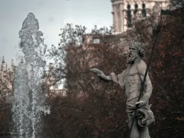 Fountain of Neptune statue with a crowned bearded figure holding a trident beside a strong water jet.