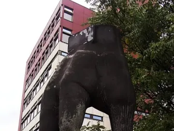 The Hand with Watch sculpture, a dark weathered hand mounted on a graffiti-covered pedestal in an urban setting.