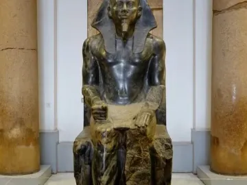 Khafre Enthroned, a dark stone statue of a seated pharaoh on an ornate throne with a falcon carved around the back.