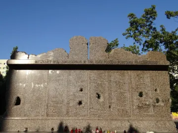 Granite Monument to Victims of the Wola Massacre with engraved Polish text and memorial candles at the base.