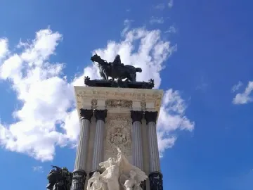 Alfonso XII Monument with a dark equestrian statue atop a multi-tiered marble base under a blue sky.