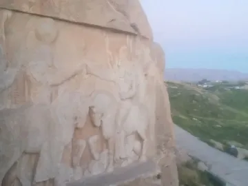 Ardashir Investiture Relief carved into a cliff, with horsemen and smaller figures overlooking green hills and a pathway.