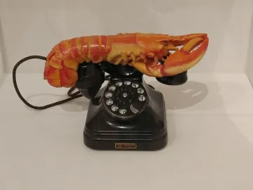 Lobster Telephone sculpture combining a black rotary phone with a bright red-orange lobster on the receiver cradle.