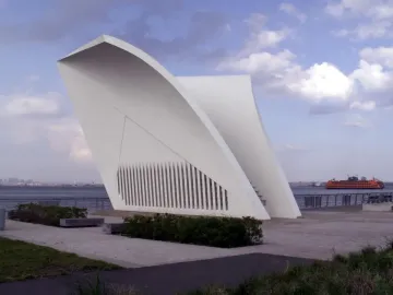 Postcards 9/11 Memorial with two white curved structures on a waterfront promenade, with a ferry and city skyline in the background.
