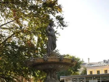 Diana Fountain with a robed female figure atop a multi-tiered stone and metal monument on a grassy lawn.